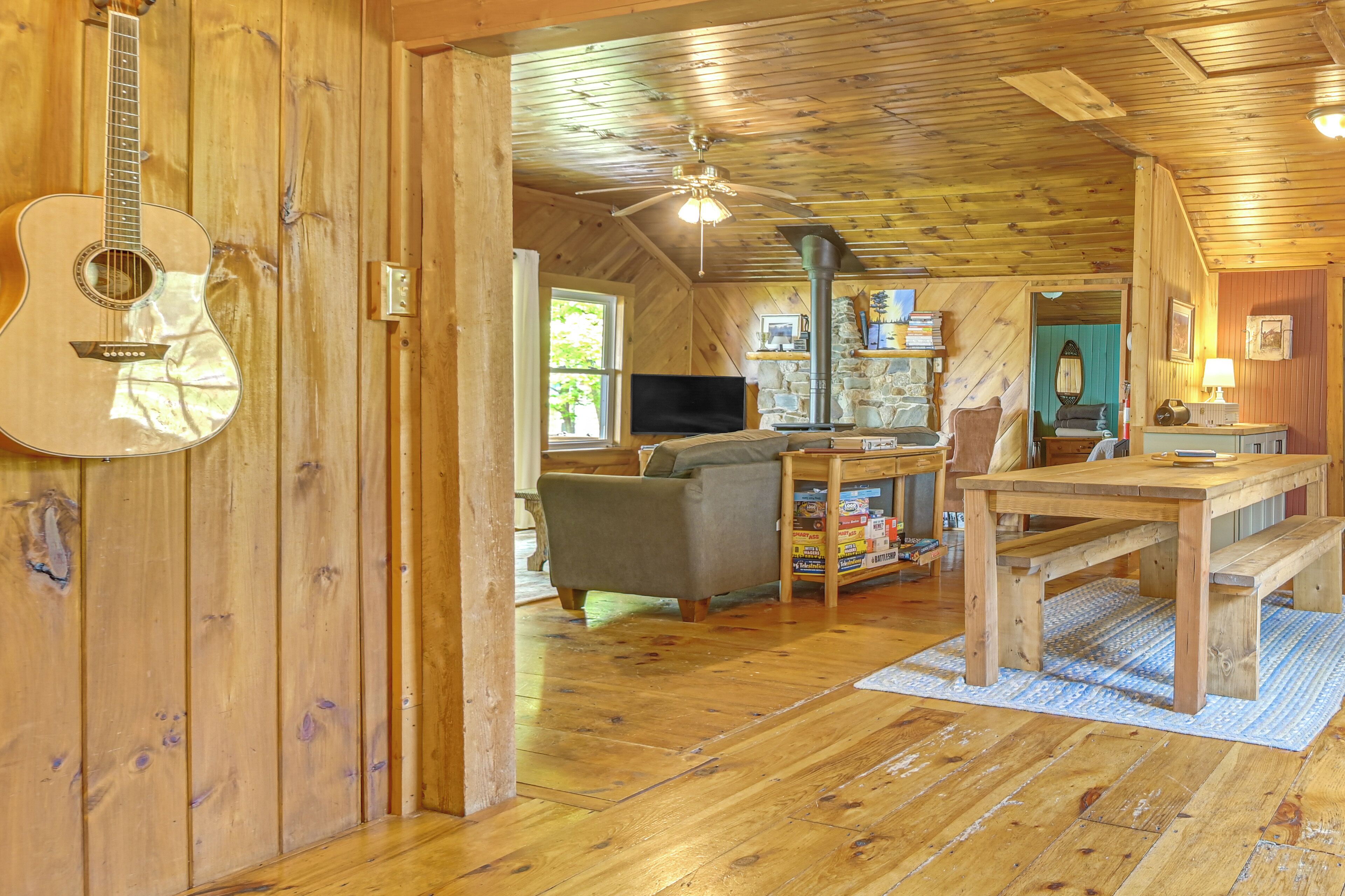 Ein gemütliches Blockhaus-Interieur mit Holzwänden, einer Gitarre, einem Sofa, einem Esstisch und einem Kamin aus Stein.