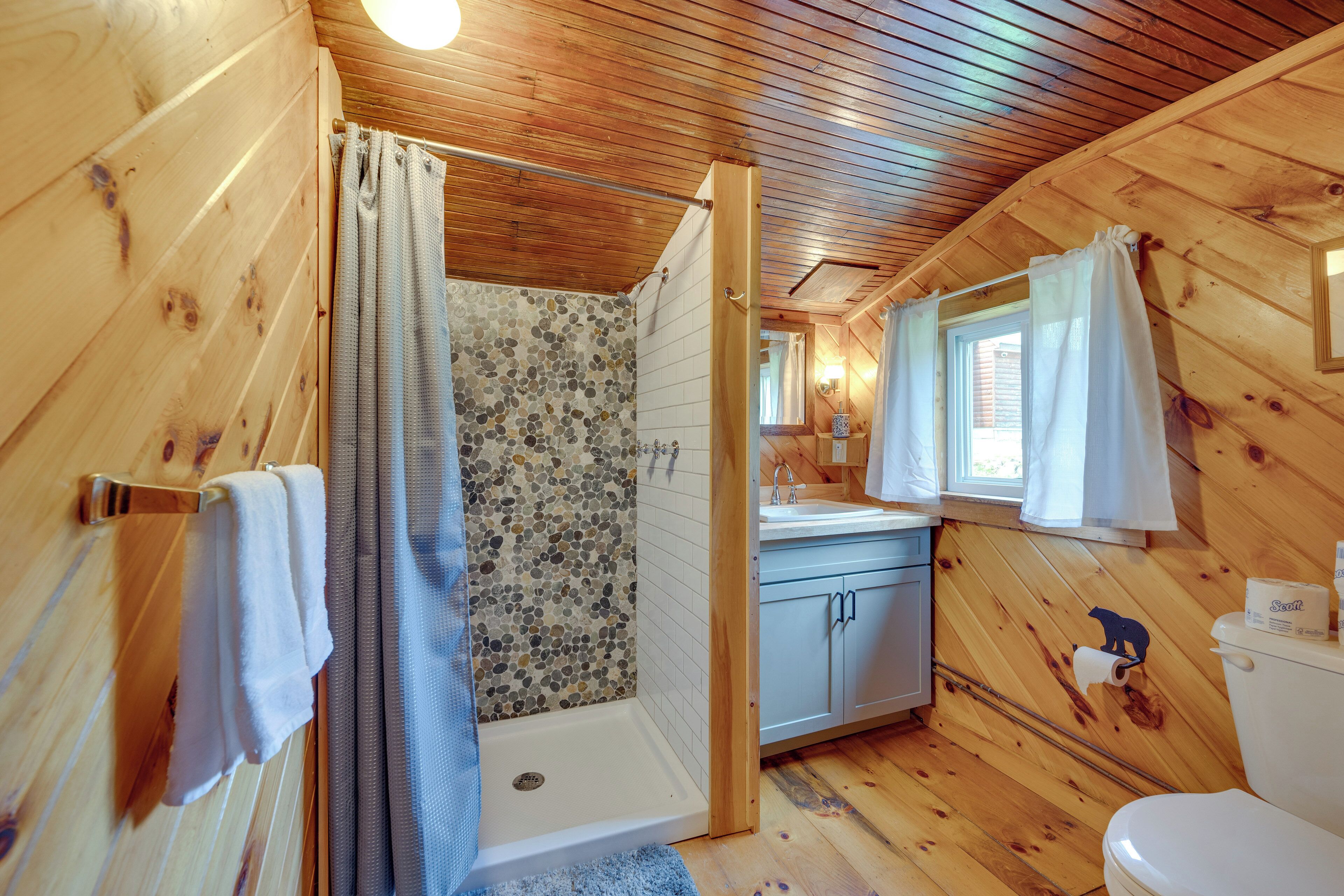 A wooden cabin bathroom with a shower, toilet, sink, and towel rack.