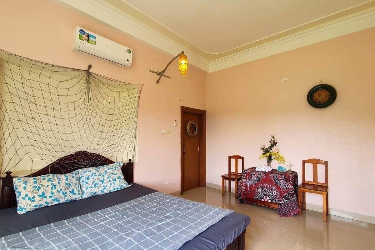 A bedroom with a bed, a mosquito net, a table with chairs, and a wall-mounted air conditioner.