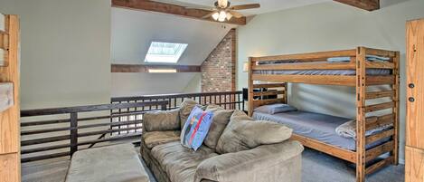 A room with a bunk bed, a sofa, and a ceiling fan.