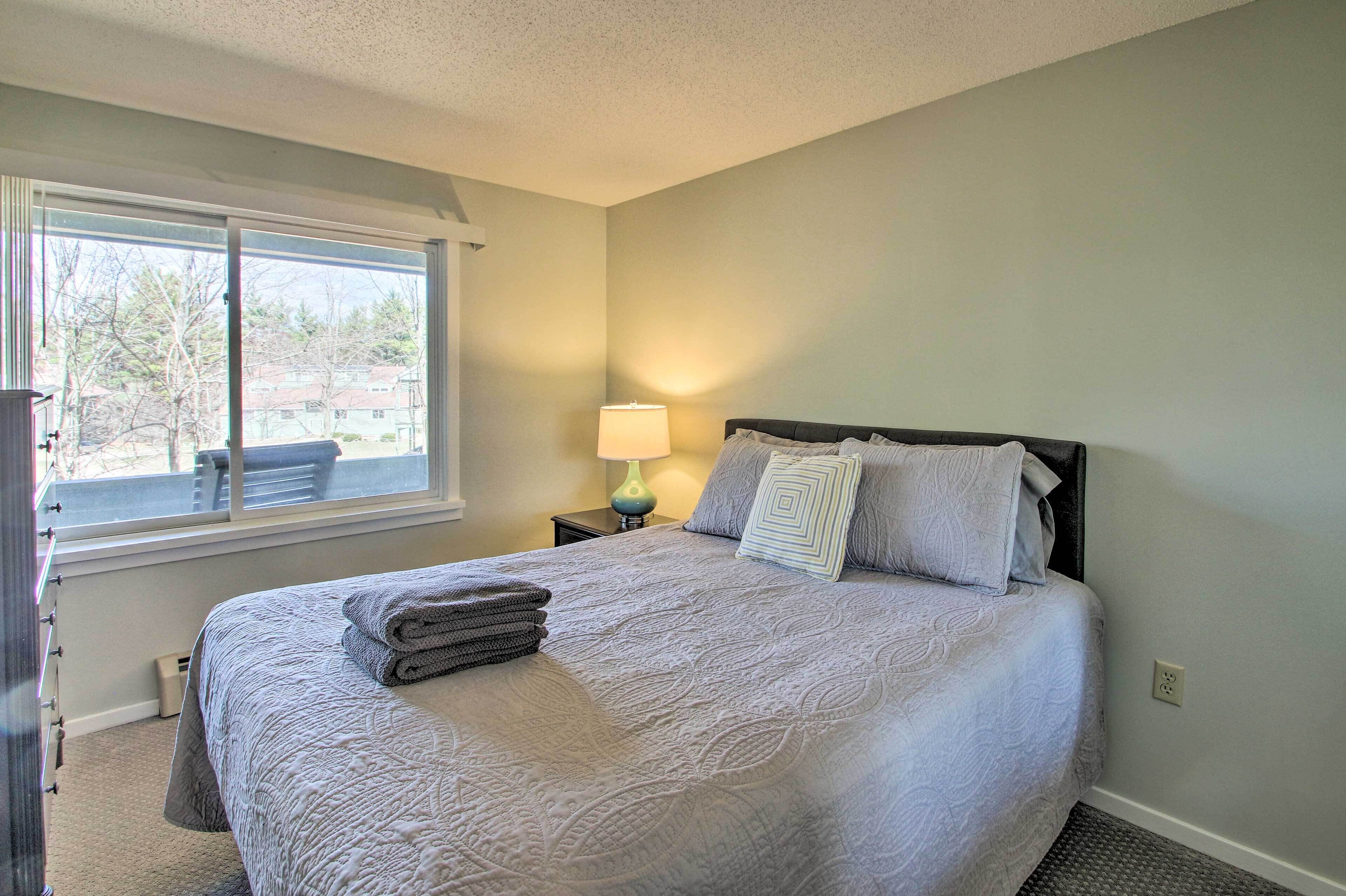 A neatly made bed with a quilt, pillows, and folded towels. A lamp is on a bedside table next to the bed.