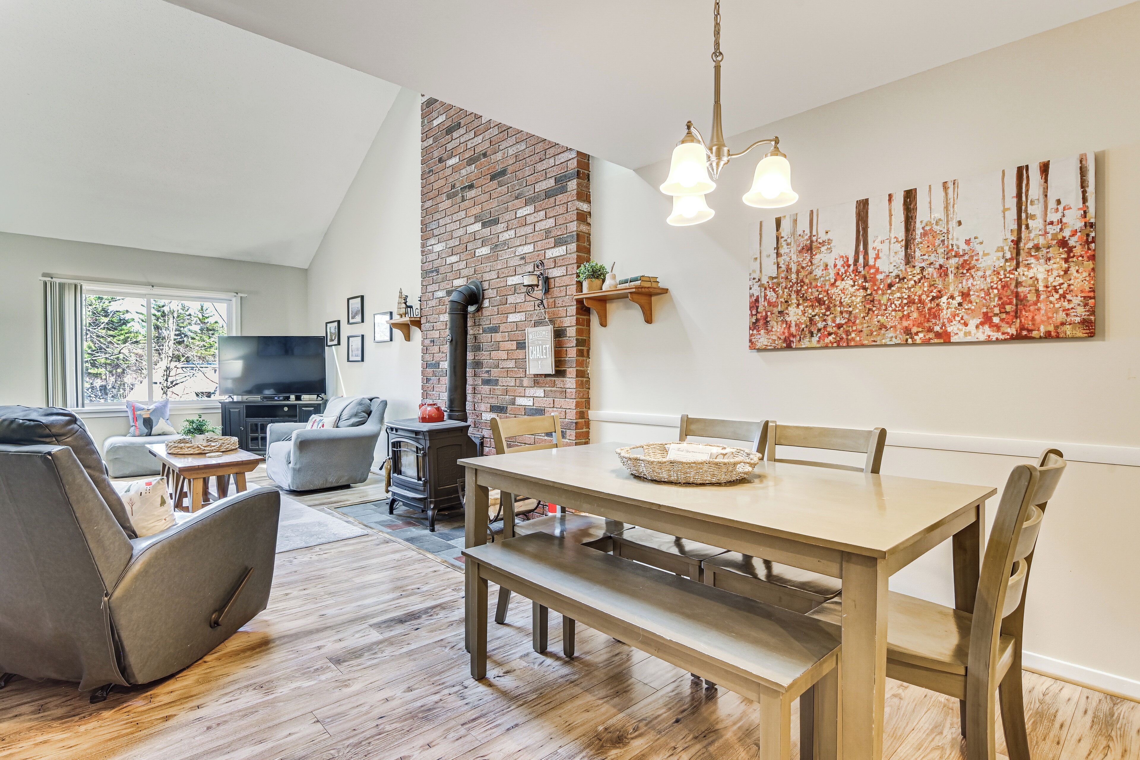 A dining area with a brick wall, wooden table, benches, and a large abstract painting.