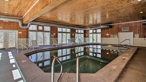 Une piscine intérieure dotée d’un plafond en bois, de grandes fenêtres et de chaises longues.