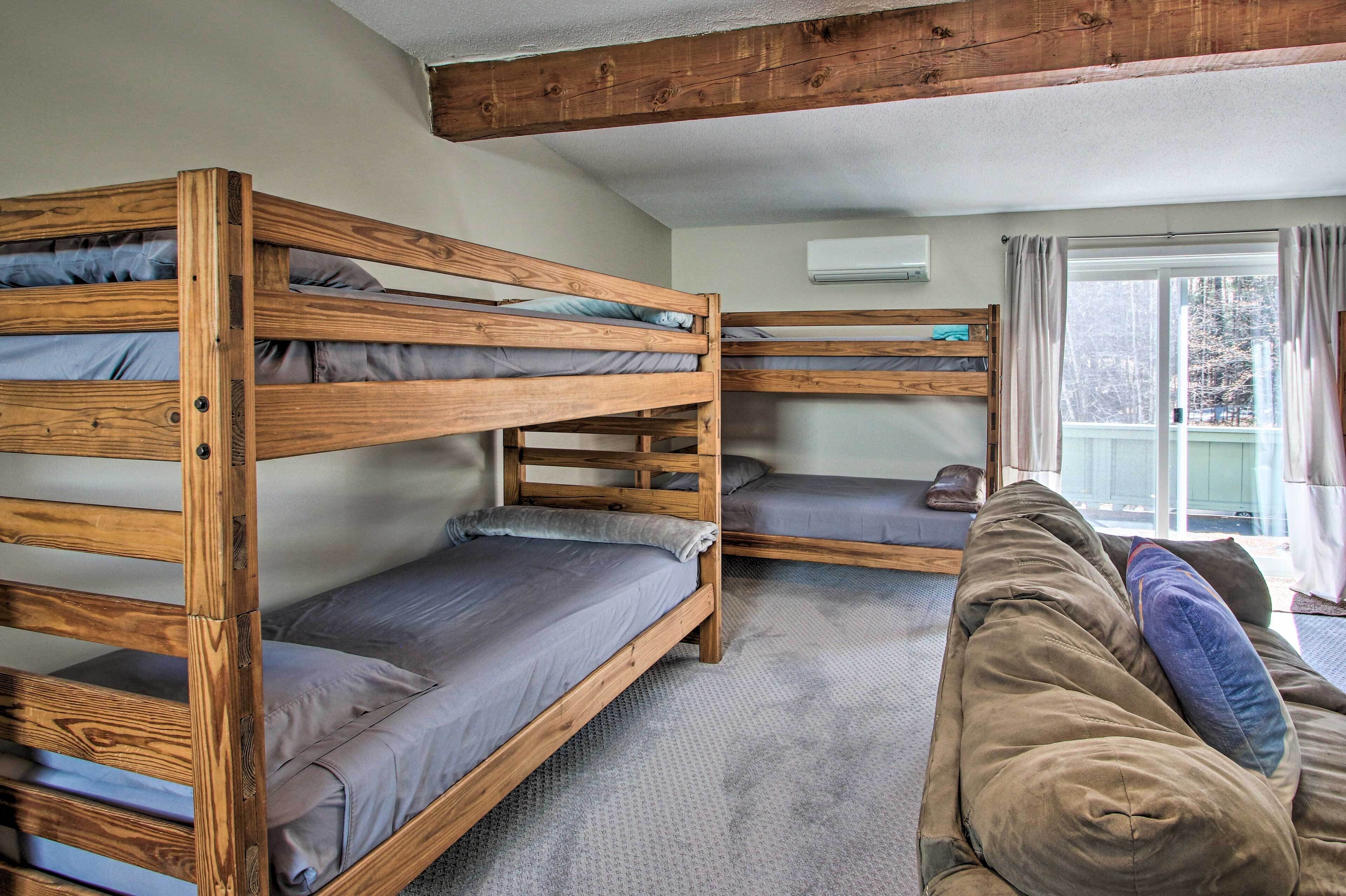 A room with three wooden bunk beds, a couch, and a window with curtains.