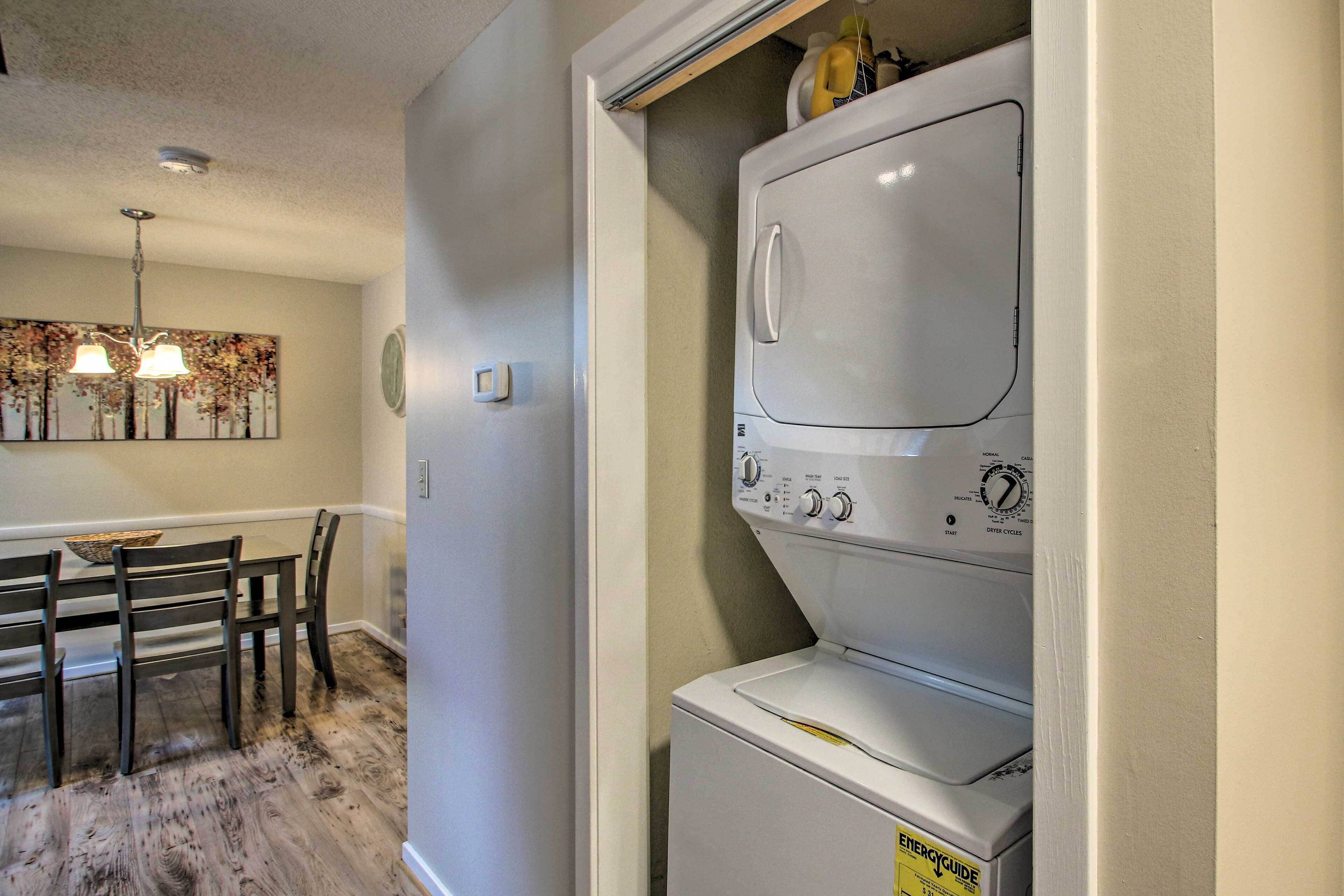 A laundry room with a stacked washer and dryer, a dining table with chairs, and a chandelier.