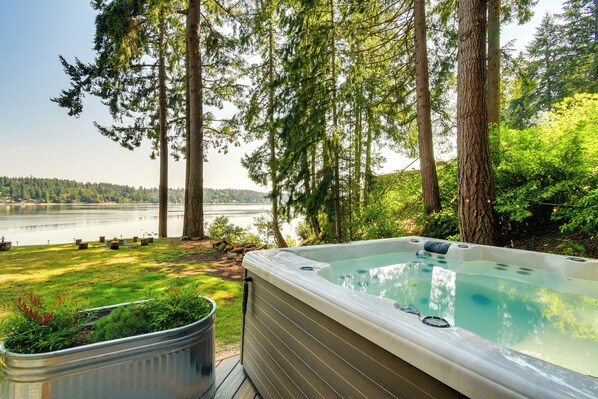 A hot tub surrounded by tall trees and a lake view. - Dreamy Wooded Cabin With Private Beach & Kayaks! (Olympia)