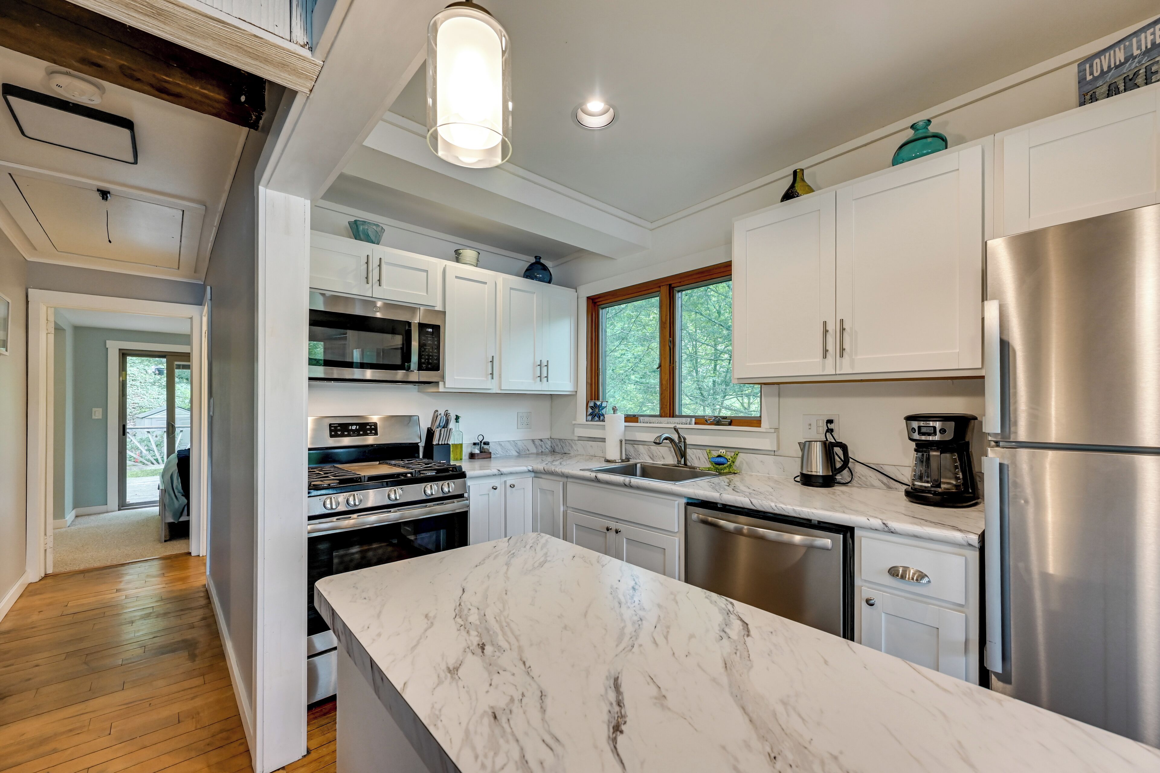 A modern kitchen with white cabinets, stainless steel appliances, and a marble countertop.