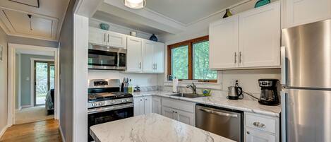 A modern kitchen with white cabinets, stainless steel appliances, and a marble countertop.