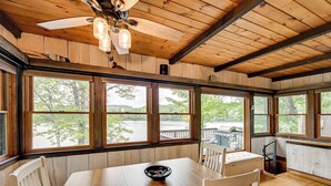A wooden interior with large windows, a dining table, and a ceiling fan. - Lakefront Granby Escape w/ Private Dock & Kayaks! (Granby)
