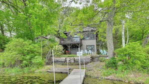 A cabin with a deck and a dock extending into a pond surrounded by dense greenery. - Lakefront Granby Escape w/ Private Dock & Kayaks! (Granby)