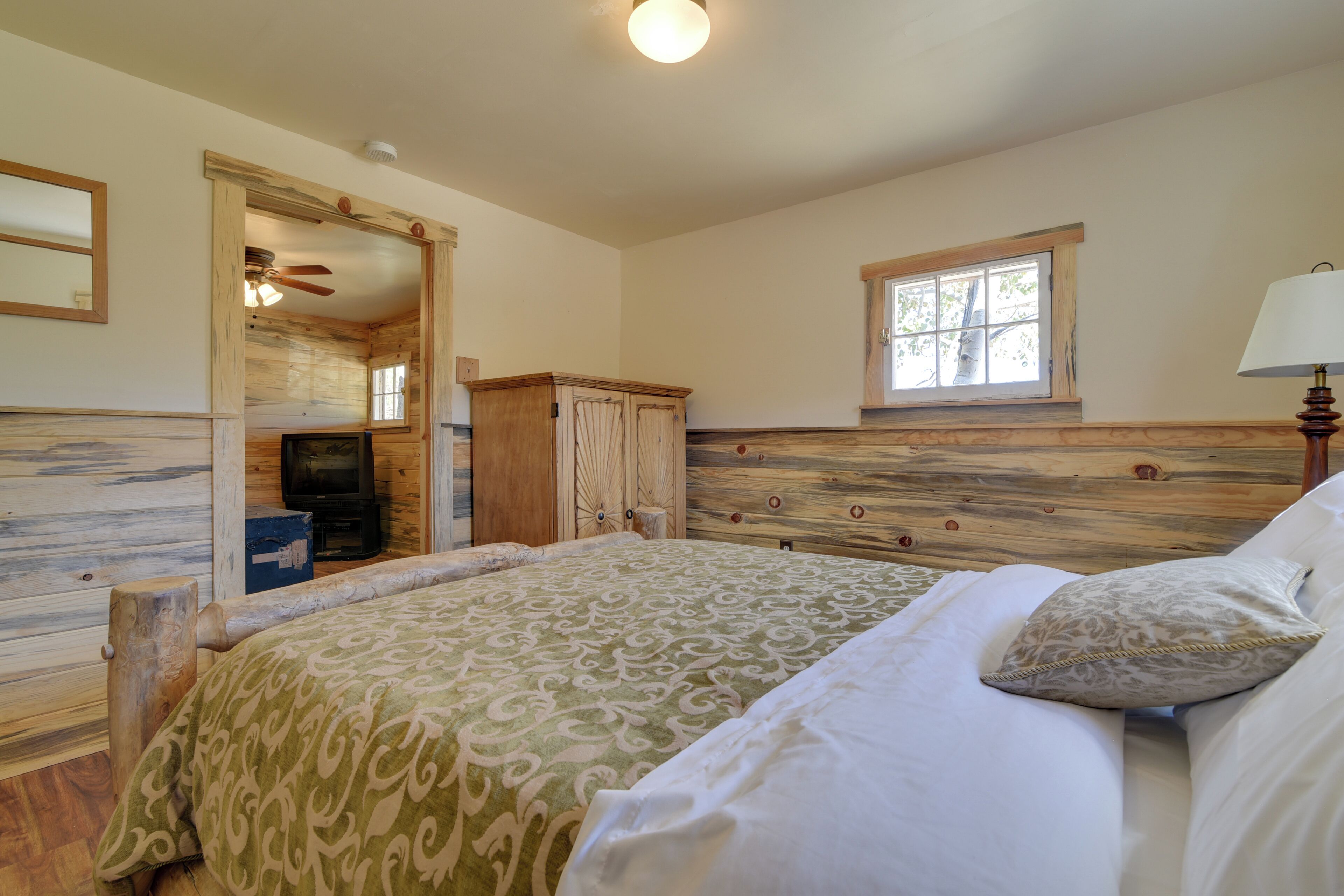 A bedroom with a wooden headboard, a bed with patterned bedding, a nightstand, and a window with a view.