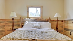 Un lit en bois avec une couvre-lit à motifs, deux lampes de chevet et une fenêtre donnant sur des arbres.