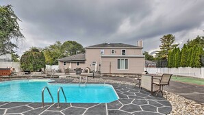 Une piscine carrelée de pierres, une terrasse avec des chaises et une maison en arrière-plan.