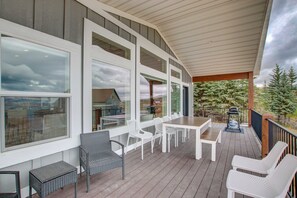 Una terraza cubierta al aire libre con zona de comedor, mobiliario de mimbre blanco y vistas a un área boscosa.