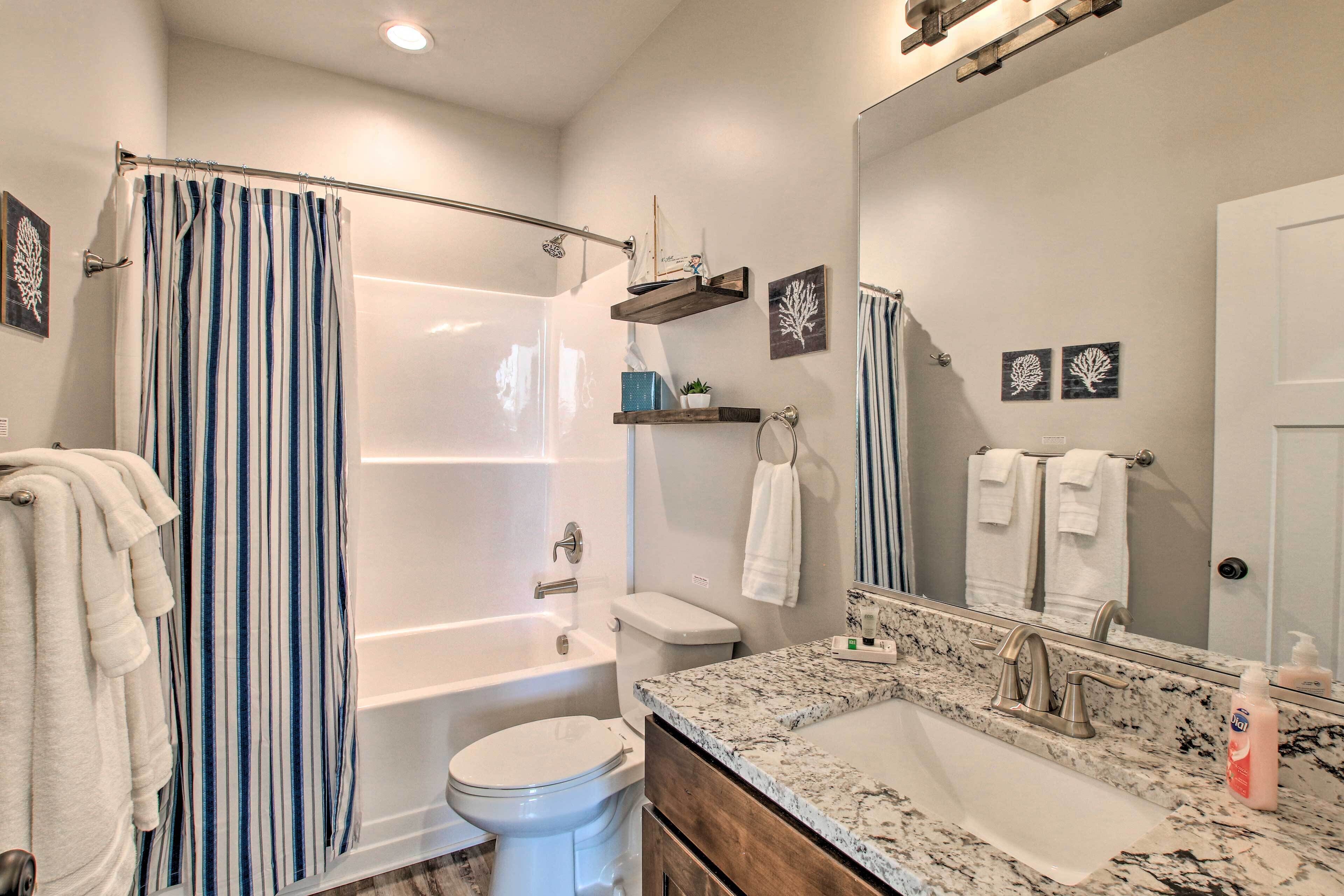 A modern bathroom with a bathtub, toilet, and sink. There are towels hanging on the wall and a shower curtain.