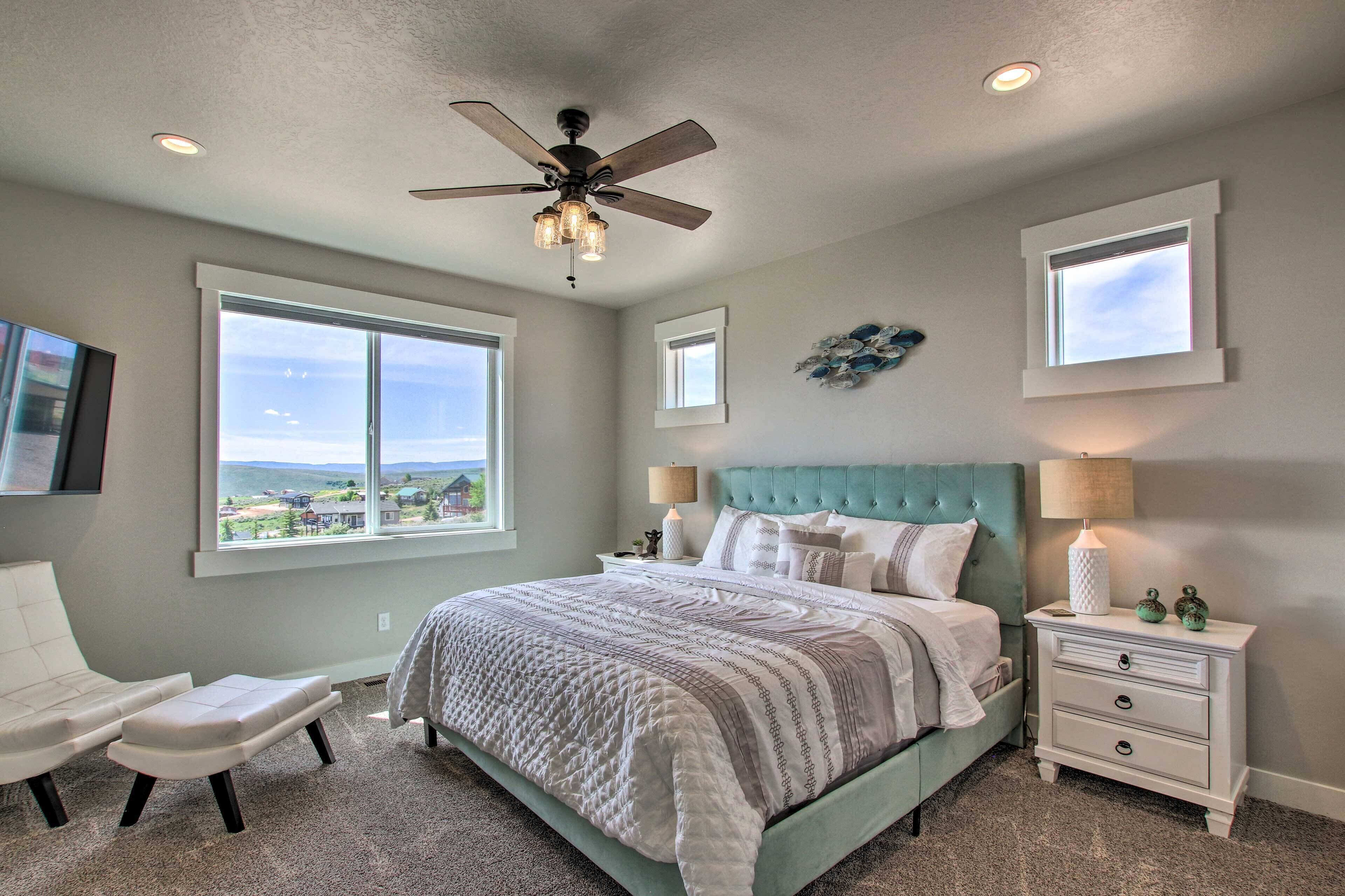 A bedroom with a bed, a chair, a nightstand, a ceiling fan, and two windows.