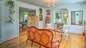 A spacious living room with a wooden floor, a red patterned sofa, a dining table with chairs, and a ceiling light fixture. - Eclectic Troy Home w/ Hot Tub - Pet Friendly! (Troy)