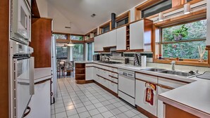 A modern kitchen with white cabinets, a built-in oven, and a large window with a view of trees. - Home With Wraparound Deck + Blue Ridge Mtn Views! (Radford)