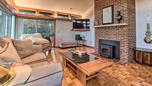 A modern living room with a fireplace, a sofa, a coffee table, and a TV mounted on the wall. - Home With Wraparound Deck + Blue Ridge Mtn Views! (Radford)