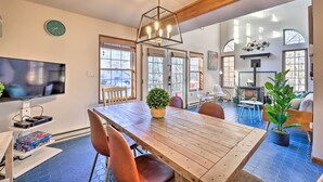 A dining area with a wooden table, chairs, and a potted plant. There is a television on a stand to the left. - Modern Poconos Gem w/ Fire Pit, Deck & Pool Access (Tobyhanna)