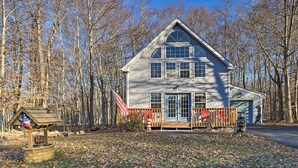 A two-story house with a porch, surrounded by a forest. - Modern Poconos Gem w/ Fire Pit, Deck & Pool Access (Tobyhanna)