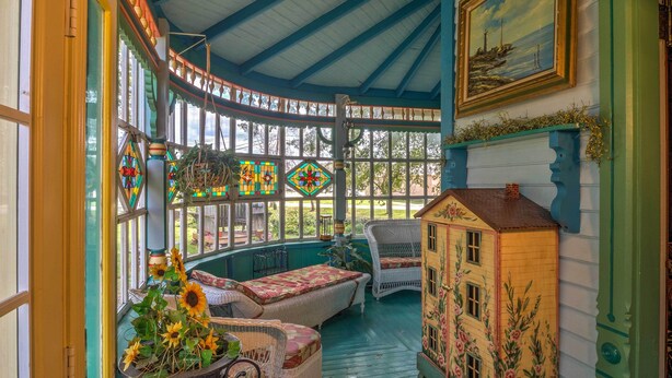 Un solárium con mobiliario de mimbre, un pequeño modelo de casa y vidrieras de colores.