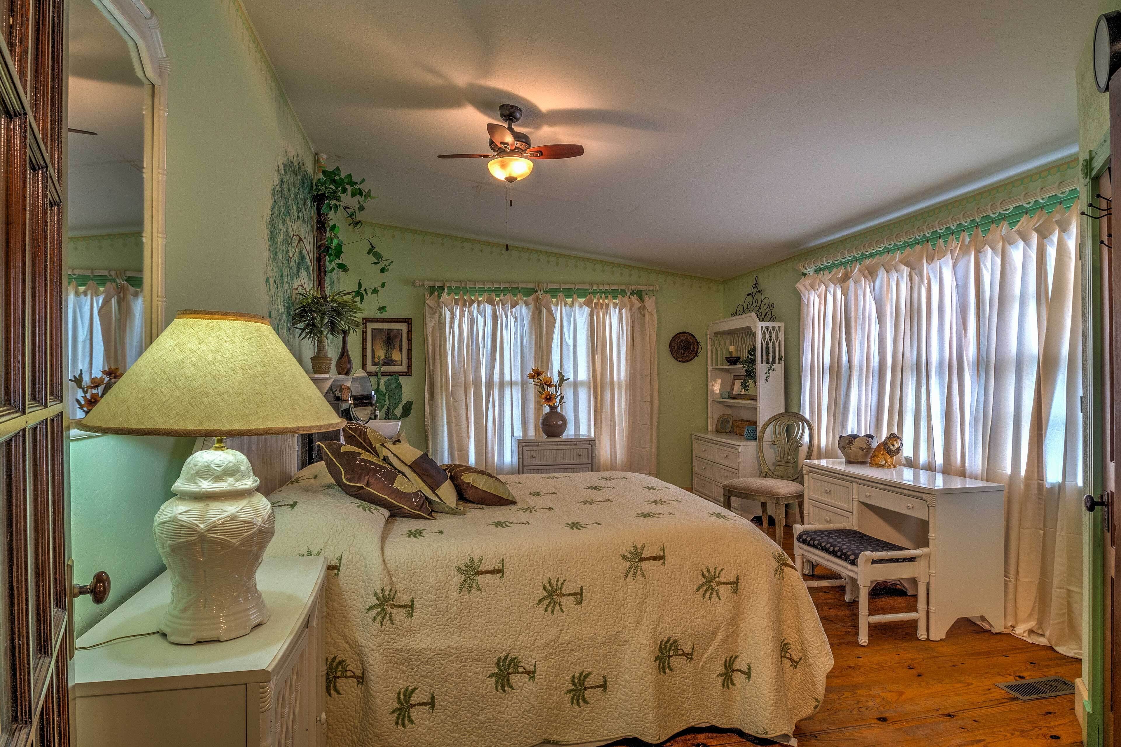 Ein Schlafzimmer mit Bett, Schreibtisch, Stuhl, Lampe und Deckenventilator.
