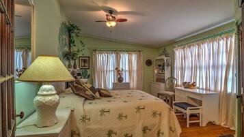 A bedroom with a bed, a desk, a chair, a lamp, and a ceiling fan.