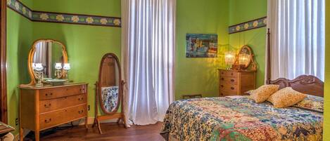 A bedroom with a wooden dresser, a bed with a floral quilt, a mirror, and a painting on the wall.