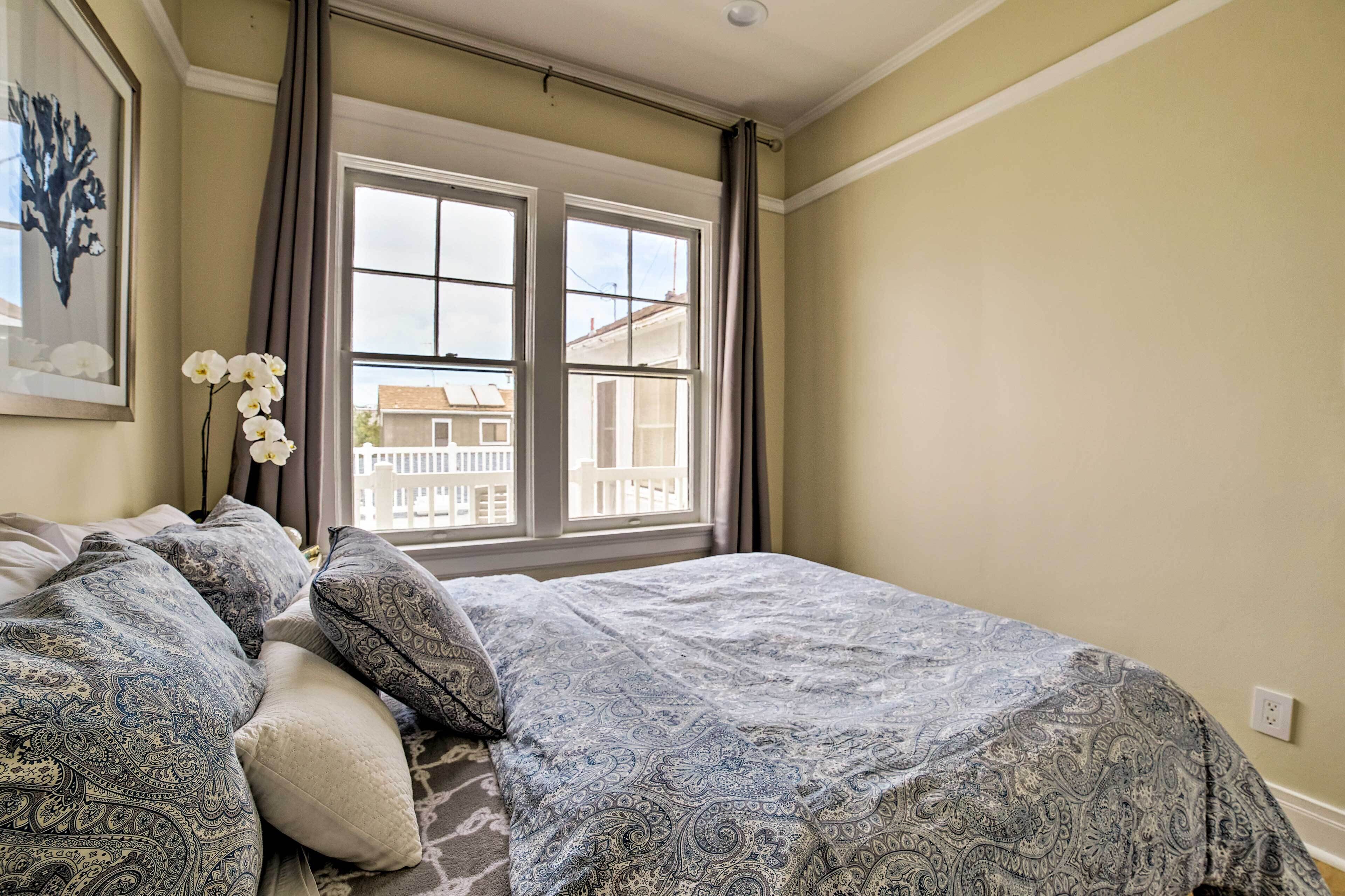 Un dormitorio con cama, ventana con cortinas y vista a edificios.