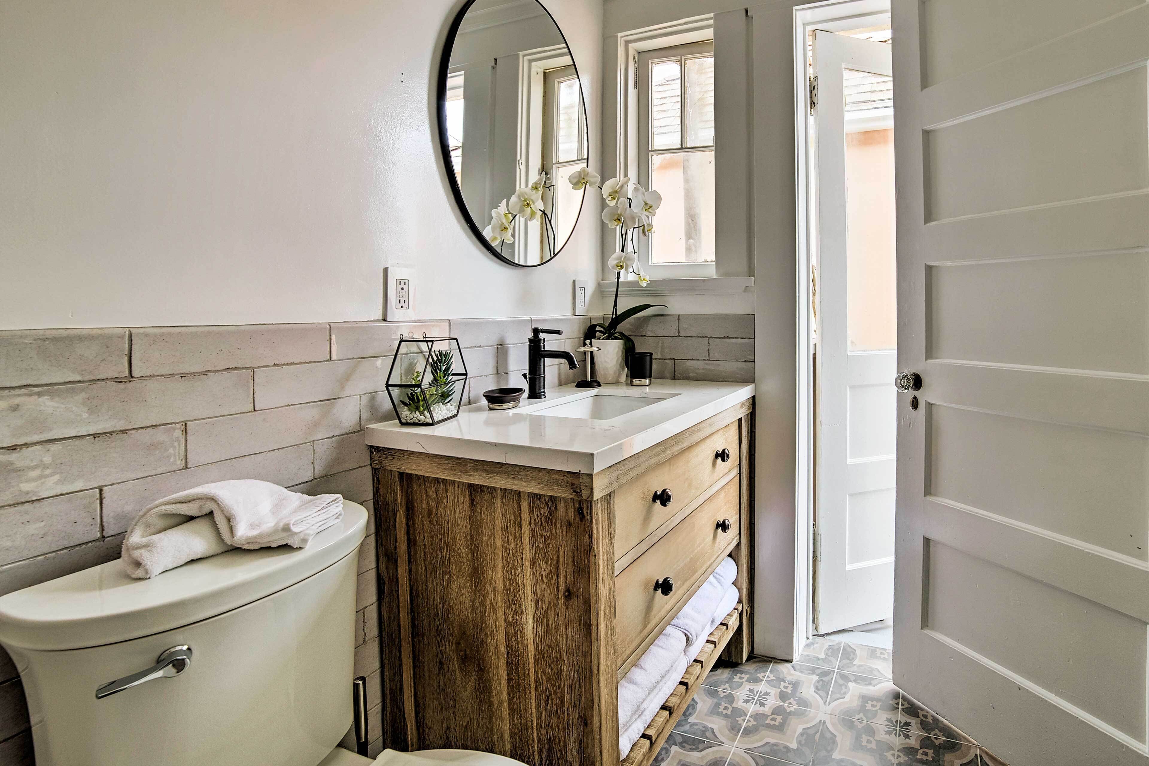 A bathroom with a toilet, sink, wooden vanity, and a mirror.