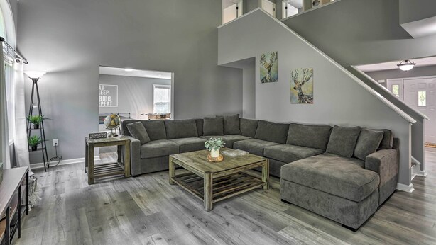 Ein modernes Wohnzimmer mit einem grauen Ecksofa, einem Holztisch und einer Treppe, die in eine obere Ebene führt.