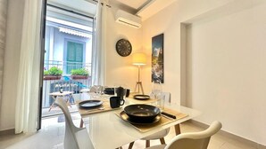 A dining area with a table set for two, a clock, and a lamp on the wall.