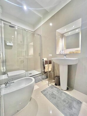 A modern bathroom with a glass-enclosed shower, a large bathtub, and a pedestal sink.