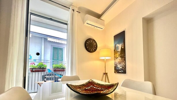 A modern dining area with a glass table, a decorative bowl, a clock, and a painting on the wall.