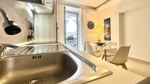 A modern kitchen with a stainless steel sink, a built-in oven, and a dining area with a table and chairs.