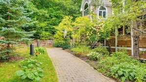 Un chemin de briques mène à une maison entourée d’une végétation luxuriante et délimitée par une clôture en bois.