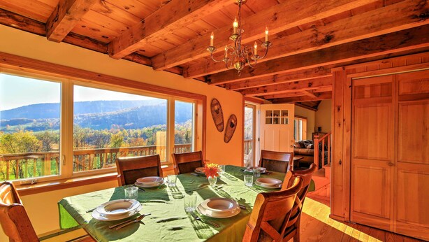 A dining area with a wooden ceiling, large windows with a view of the mountains, and a table set for four.