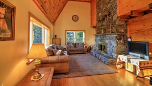 A cozy living room with a stone fireplace, wooden ceiling, and a television on a table.