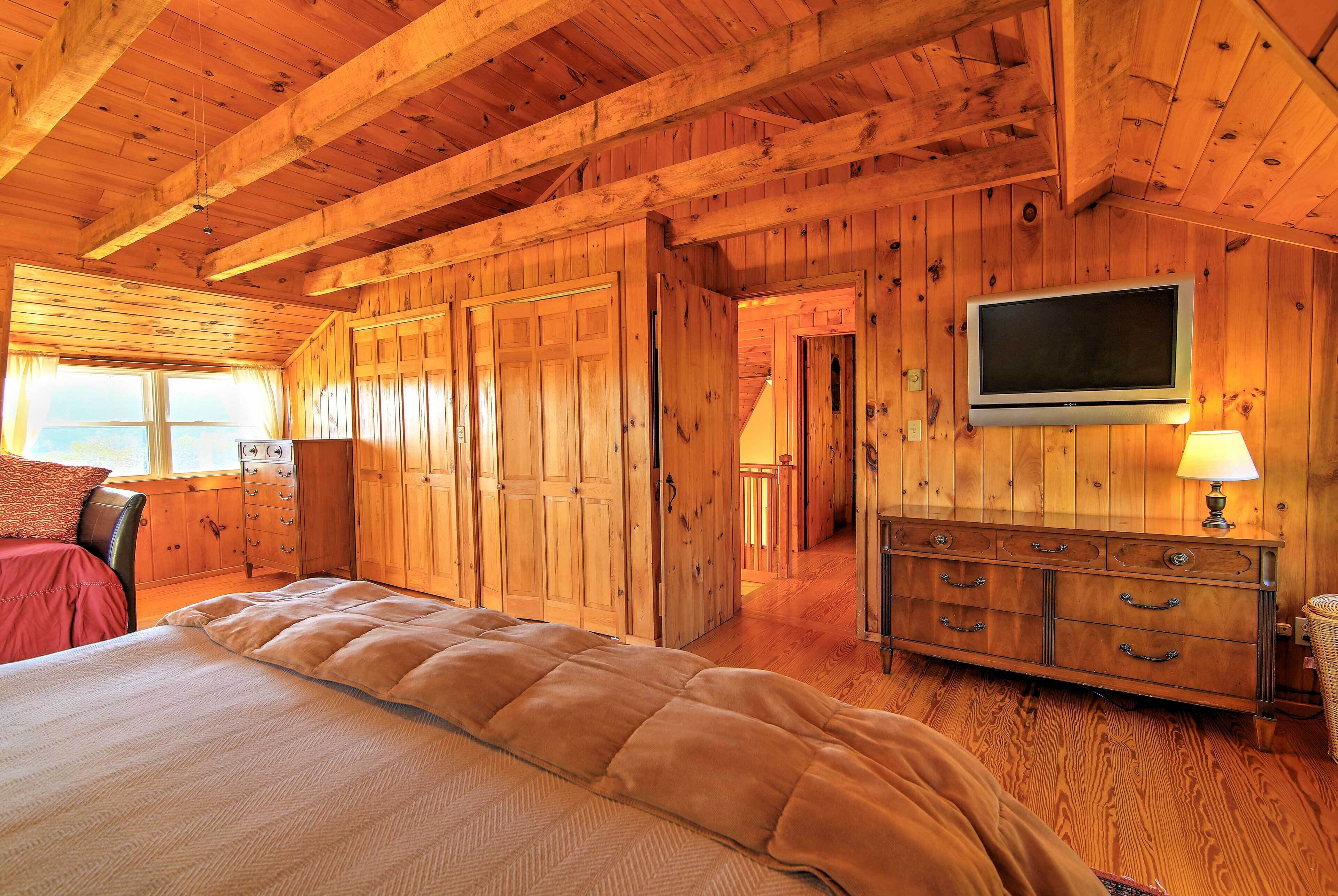 A wooden cabin interior with a bed, dresser, and TV.