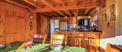 A wooden interior with a dining table set for two, a kitchen area, and a view of the outdoors.
