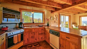 A kitchen with wooden cabinets, a stove, a dishwasher, and a window with a view of trees.