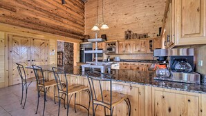 A log cabin kitchen with a central island, bar stools, granite countertops, and wooden cabinets. - Grand Mountain Retreat in Angel Fire w/ Game Room! (Eagle Nest)
