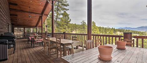Una terraza de madera con mobiliario exterior, una parrilla y vistas a un paisaje boscoso.