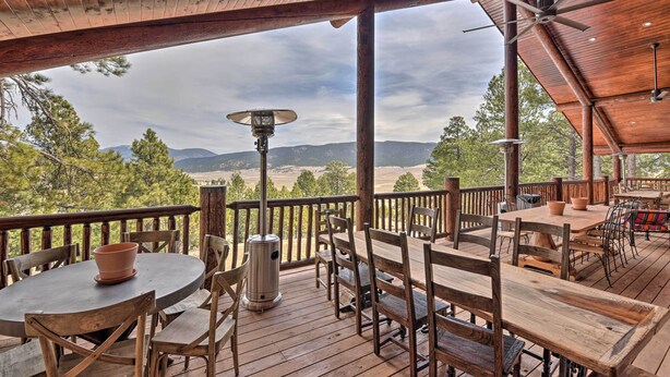 A wooden deck with tables and chairs, overlooking a mountainous landscape. - Grand Mountain Retreat in Angel Fire w/ Game Room! (Eagle Nest)