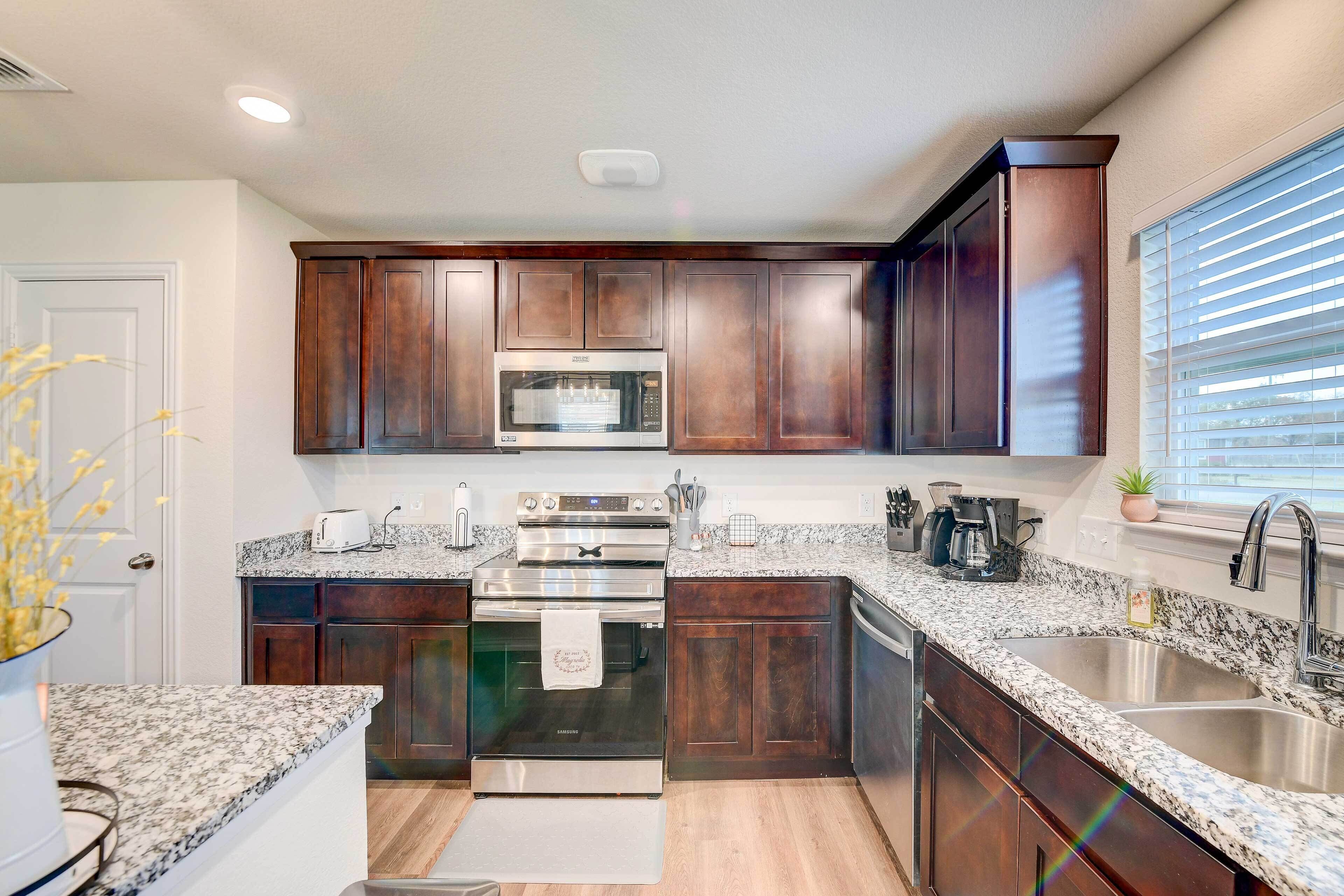 A modern kitchen with dark wood cabinets, stainless steel appliances, granite countertops, and a window with blinds.