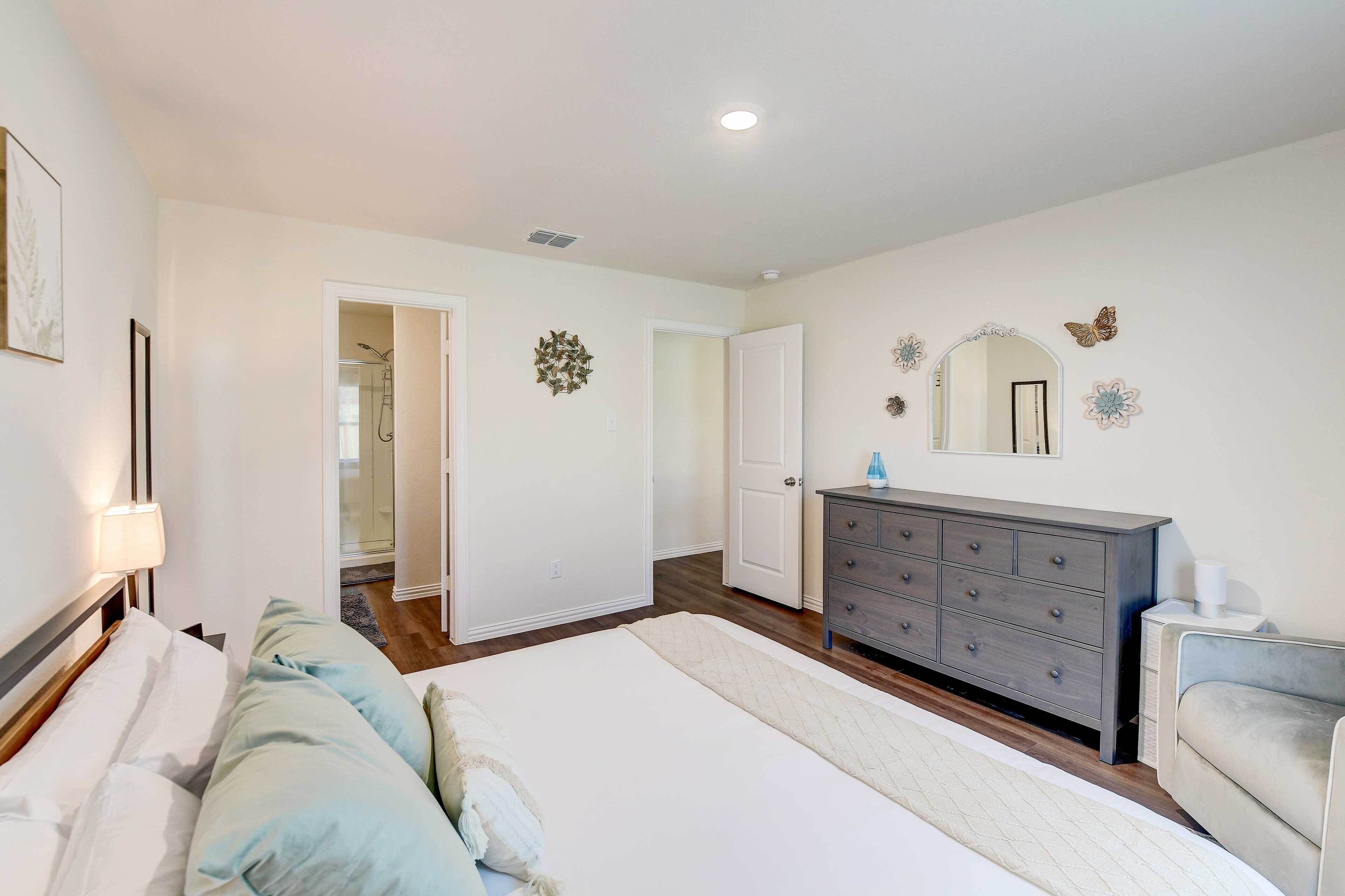 A bedroom with a large bed, a dresser, a mirror, and a door leading to a bathroom.