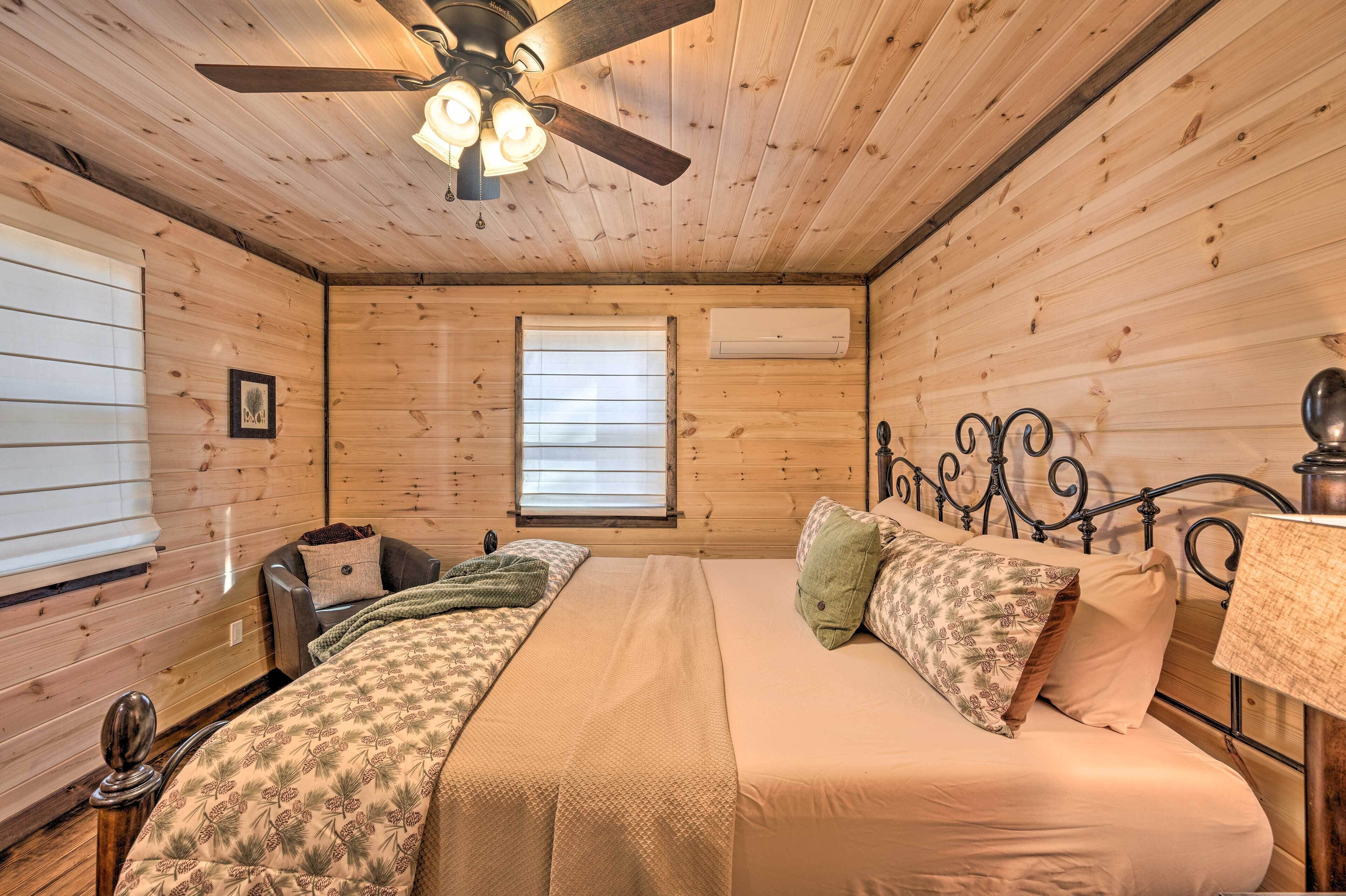 A wooden cabin bedroom with a bed, a chair, a ceiling fan, and a window.