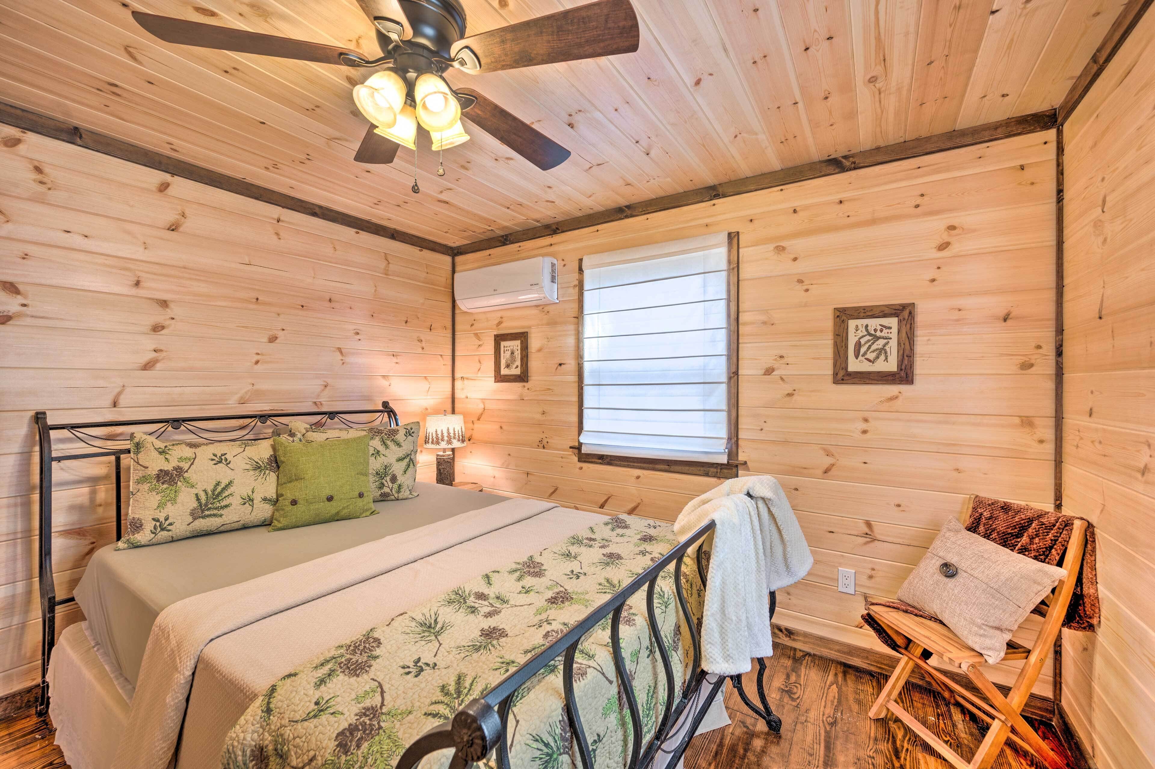 Ein Schlafzimmer in einer Holzhütte mit einem Bett, einem Sessel, einem Deckenventilator und einem Fenster mit Jalousien.