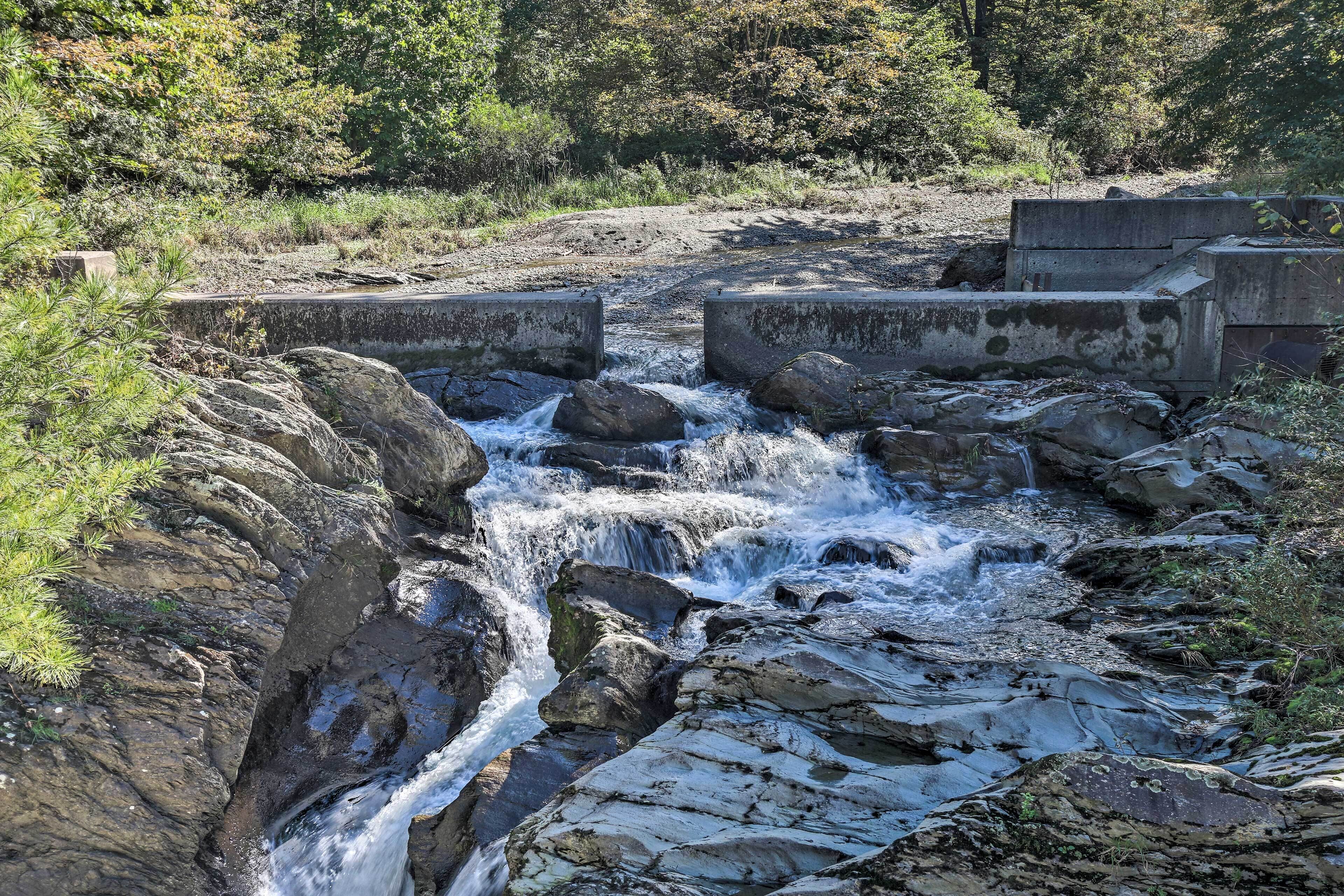 A natural stream flowing over rocks with a concrete barrier in the background.